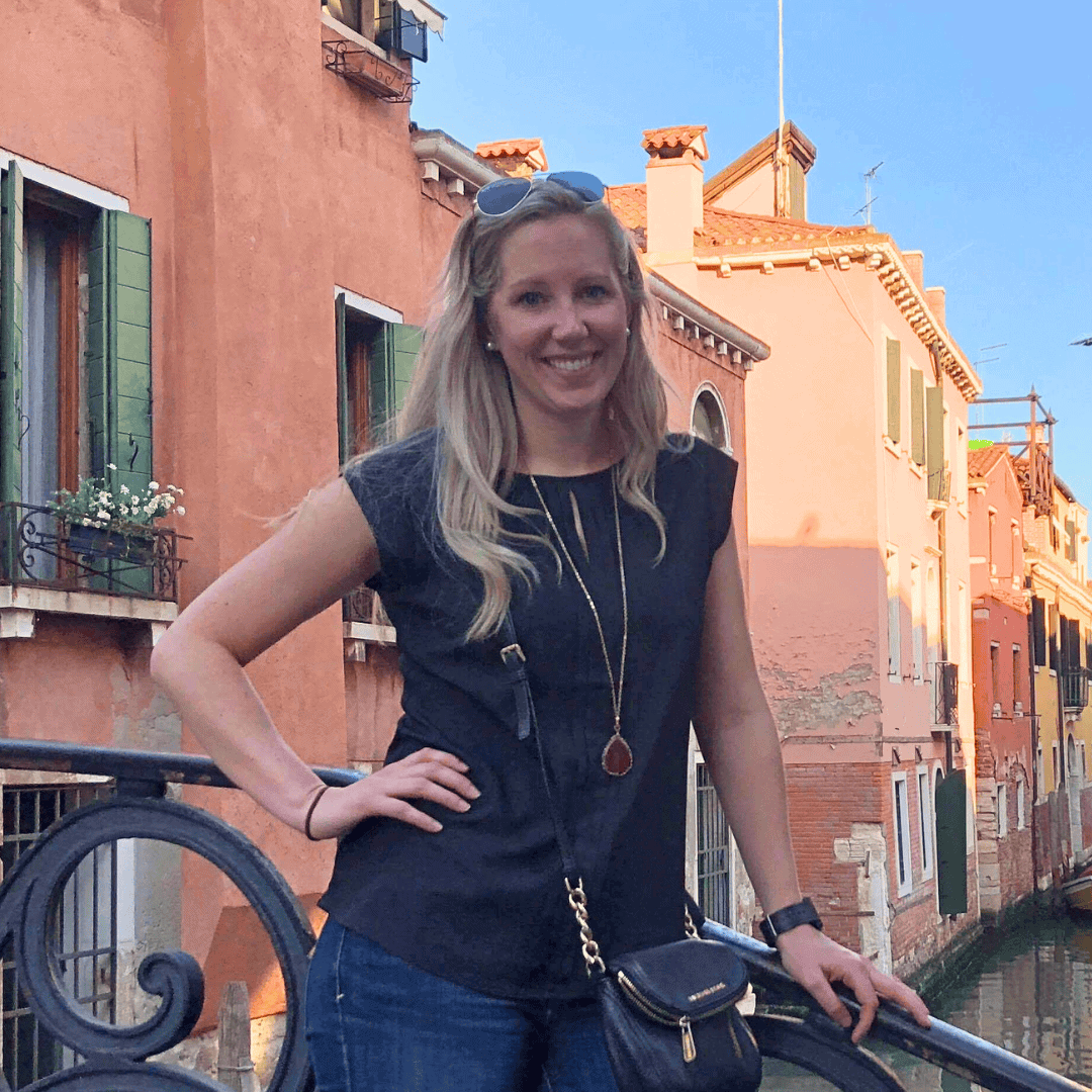 Smiling woman standing by Venice canal with colorful buildings.
