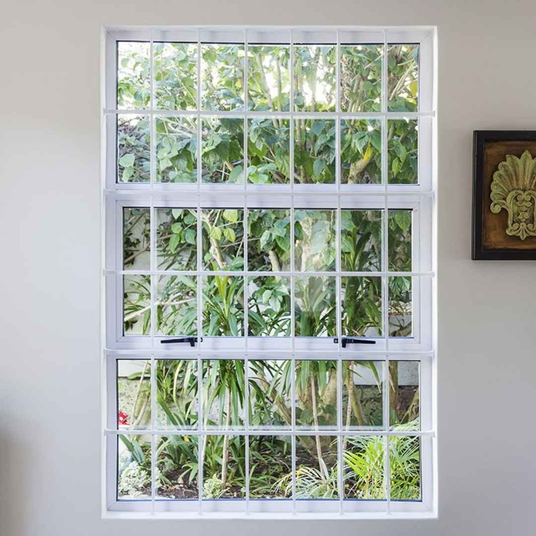 Cottage pane burglar bars installed on a tall window, set against the backdrop of a home's outside area.
