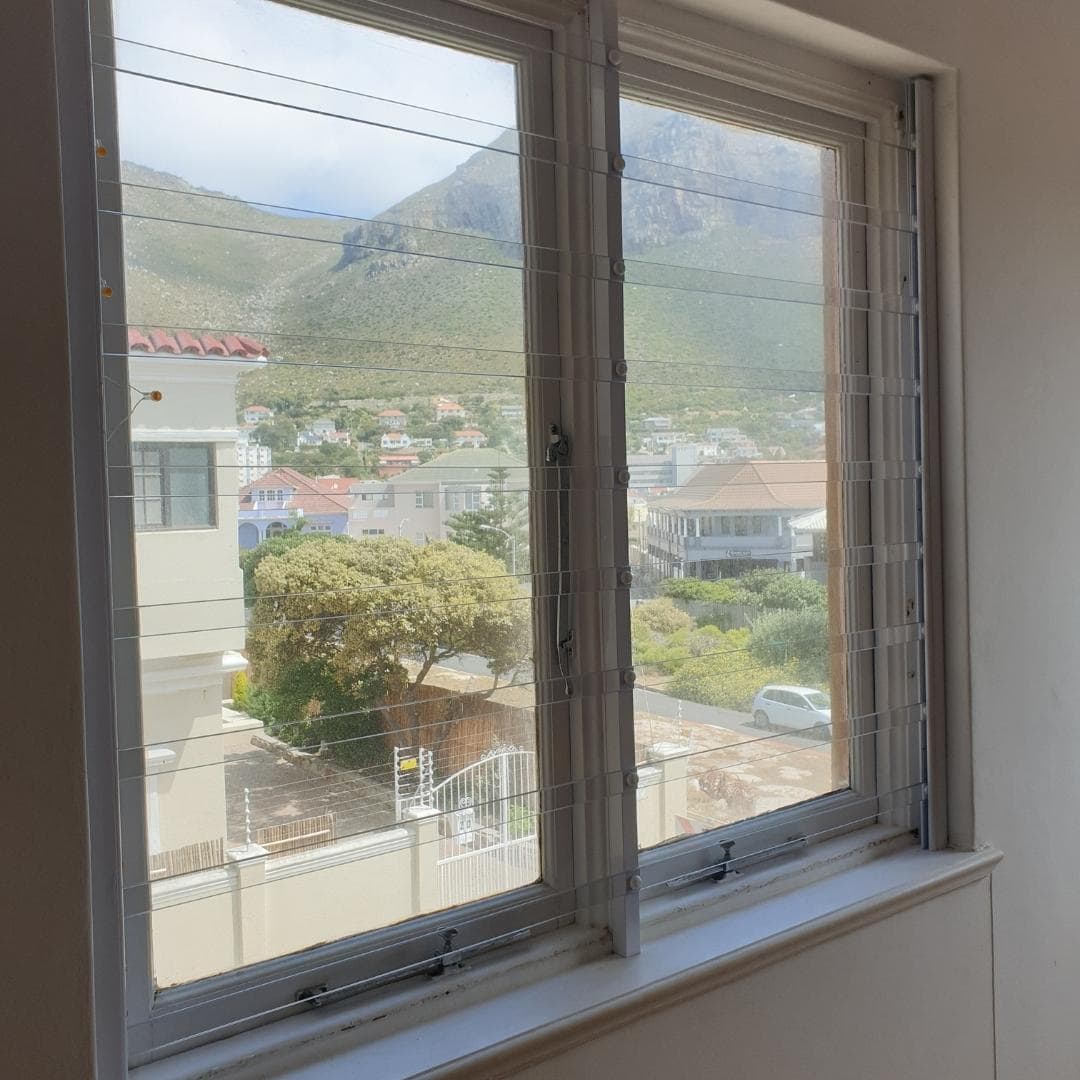 Upper-storey white timber window overlooking a coastal suburb and mountain backdrop, secured by clear bars burglar bars for discreet residential protection.
