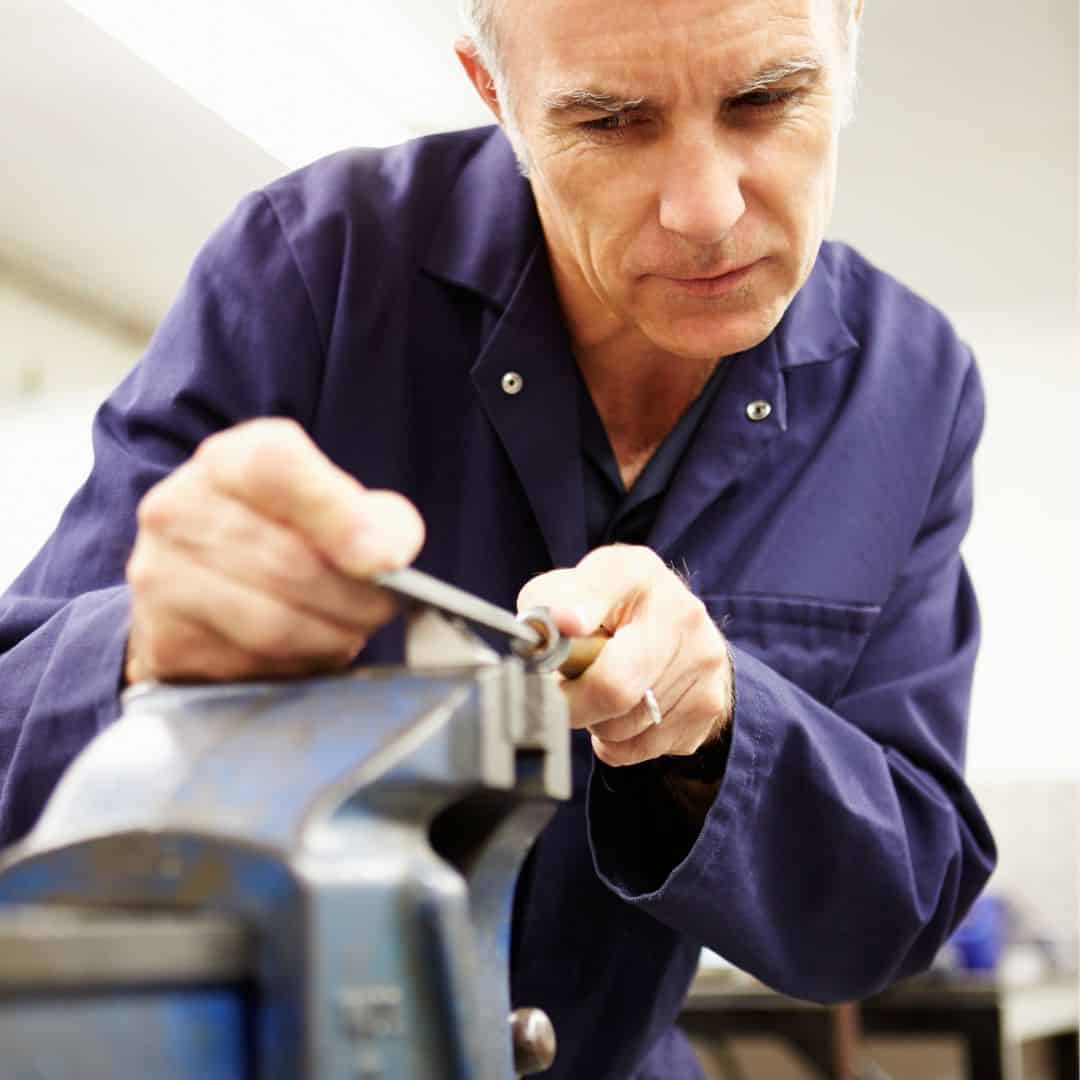 Worker sharpens the cut rod in a vise with a metal file 