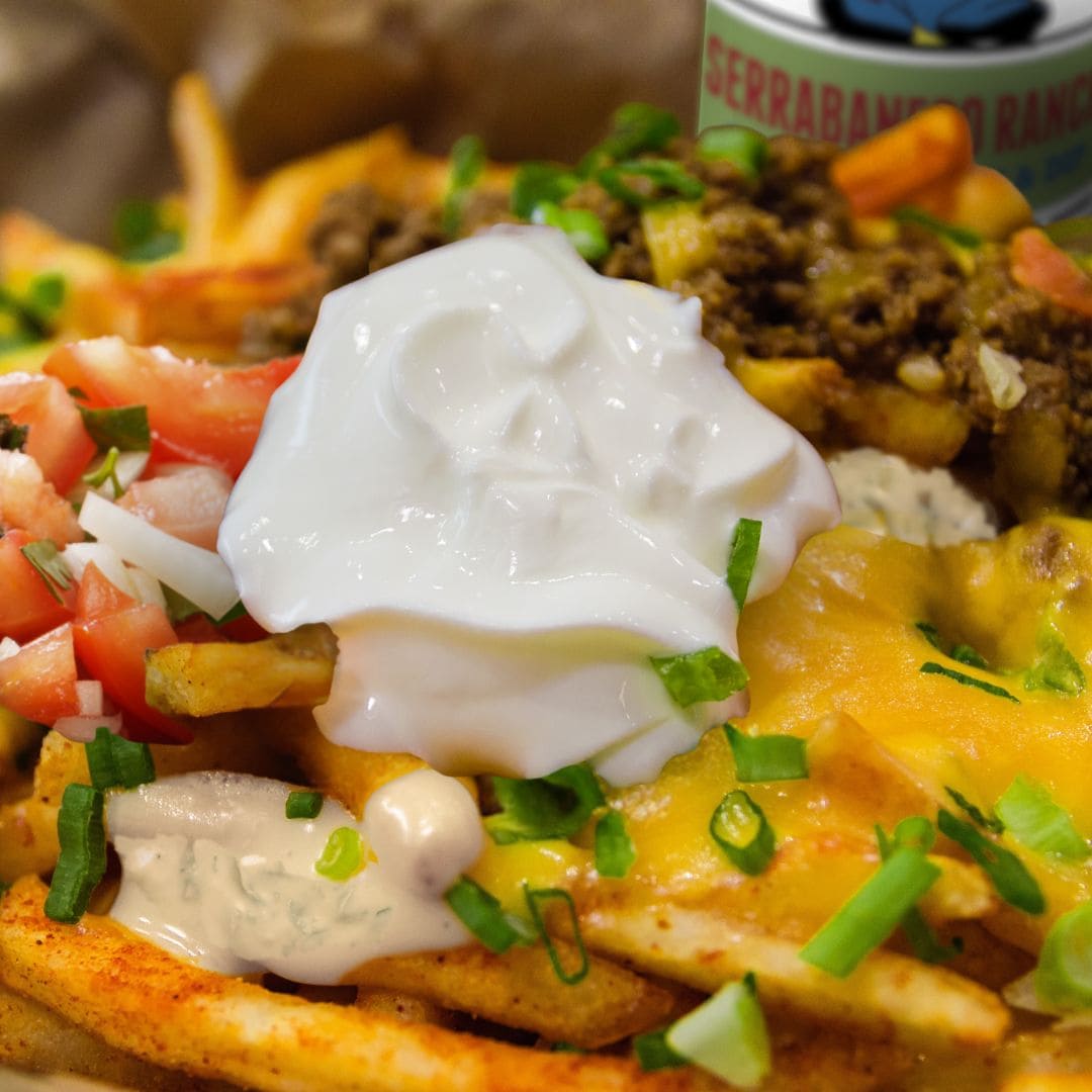 A brimming portion of Secret Aardvark Nacho Fries covered in melted cheddar cheese, a dollop of sour cream, and Serrabanero Spicy ranch Dressing & Dip
