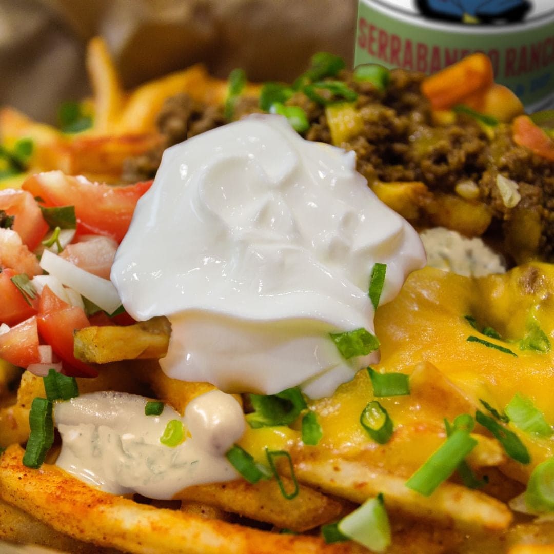 A brimming portion of Secret Aardvark Nacho Fries covered in melted cheddar cheese, a dollop of sour cream, and Serrabanero Spicy ranch Dressing & Dip