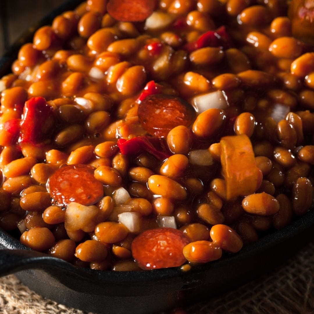 Skillet of baked beans with sliced sausage and onions.