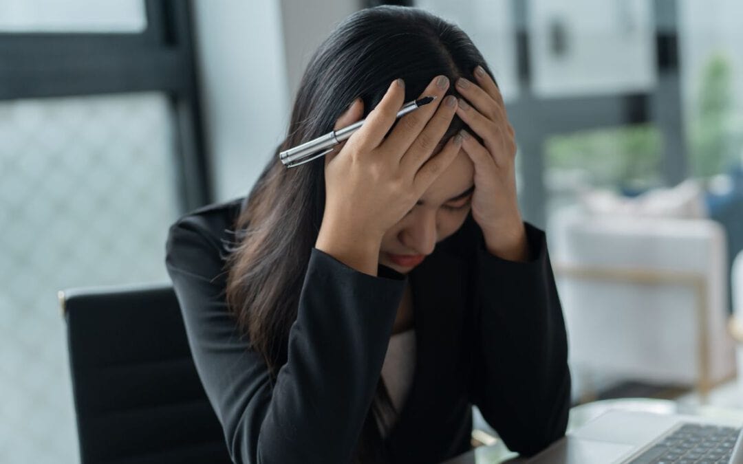 Frau im Büro gestresst, hält Kopf mit Händen, Arbeit belastet.