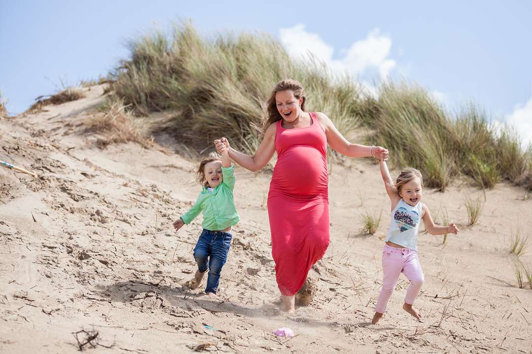 Hoogzwangere moeder rent een duin af met haar twee kinderen hand in hand