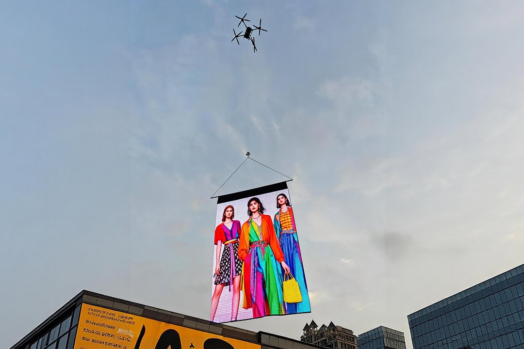 Hovering flying LED display featuring fashion models advertisement above urban buildings during daytime