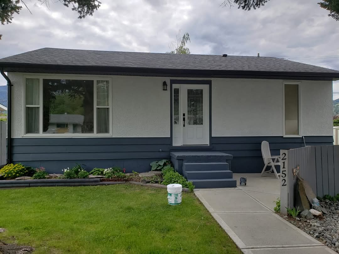 Fresh exterior paint job by Kameliun Painters in Merritt, BC, featuring a modern two-tone design with dark blue trim and white stucco finish on a single-level home.