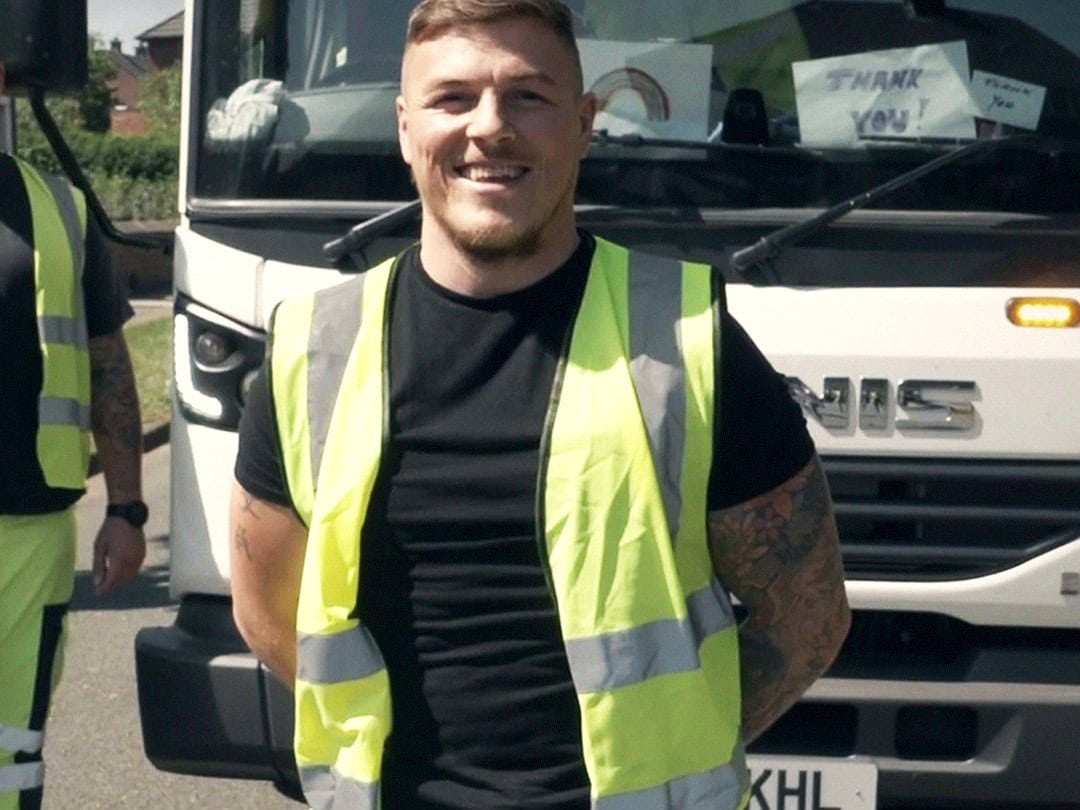 A refuse collector in high-visibility clothing in front of a council wagon