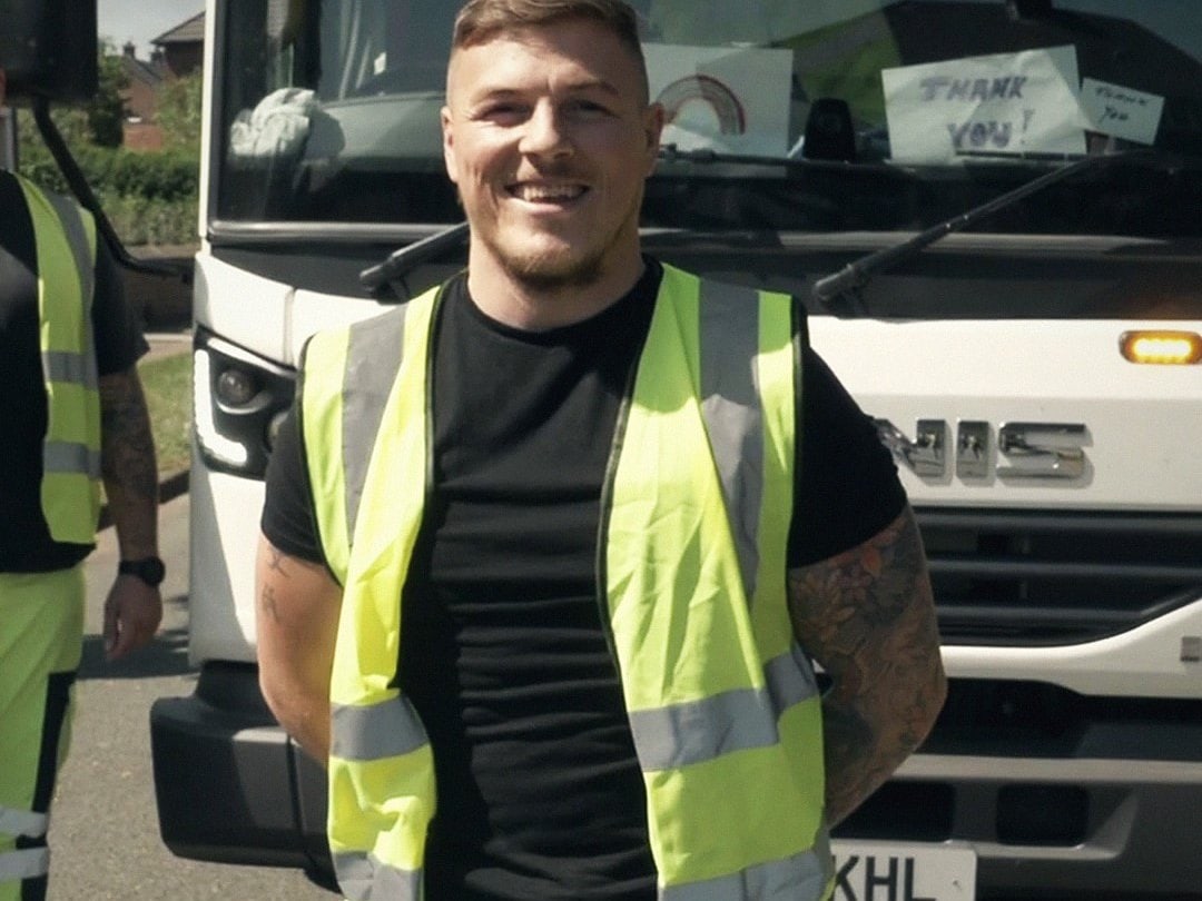 A refuse collector in high-visibility clothing in front of a council wagon