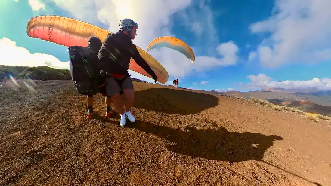 Piloto de parapente con la vela inflada sobre él en el despegue, en terreno volcánico del norte de Tenerife