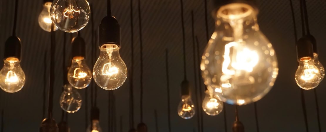 Mehrere Glühbirnen hängen an langen Kabeln von der Decke und leuchten in warmem Licht. Das Bild symbolisiert das fachgerechte Anschließen von Lampen, elektrische Sicherheit und Beleuchtungstechnik.