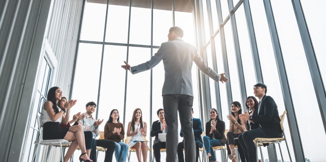Persone in azienda che partecipano a una presentazione di un collega e lo applaudono