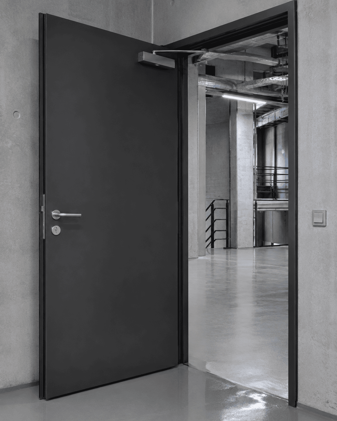 Dunkelgraue Metalltür von Stahl- und Metallbau Drost mit Türschließer, leicht geöffnet in einem modernen Industrieraum.