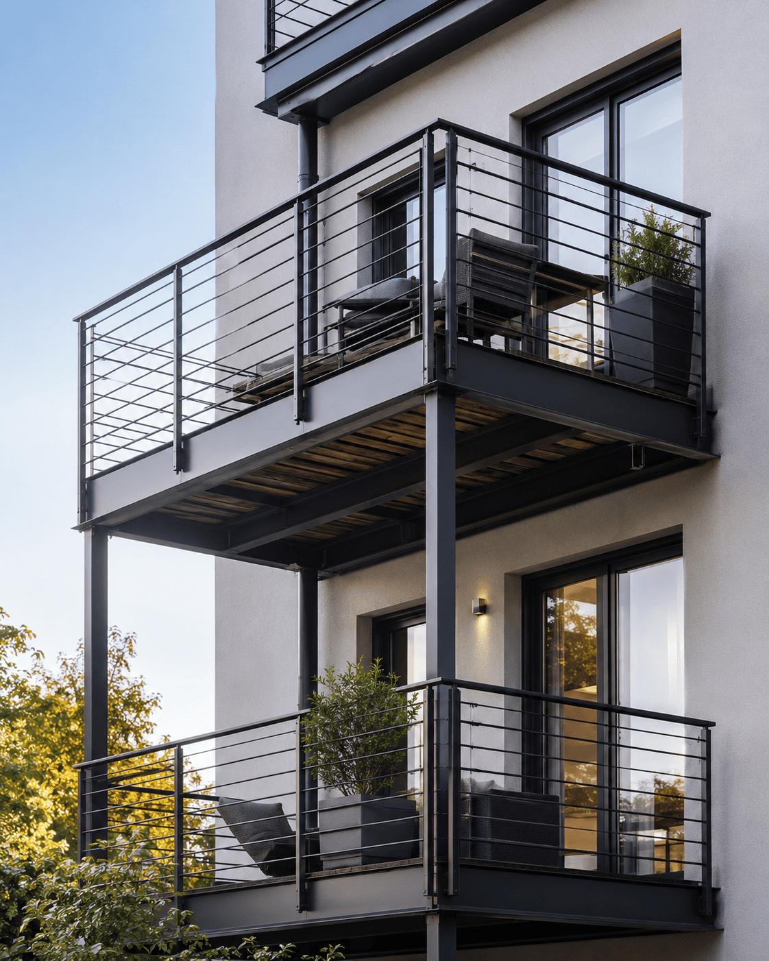 Zwei moderne Anbaubalkone von Stahl- und Metallbau Drost mit dunklem Stahlrahmen, Holzbelag und filigranem Edelstahlgeländer an einer hellen Gebäudefassade.