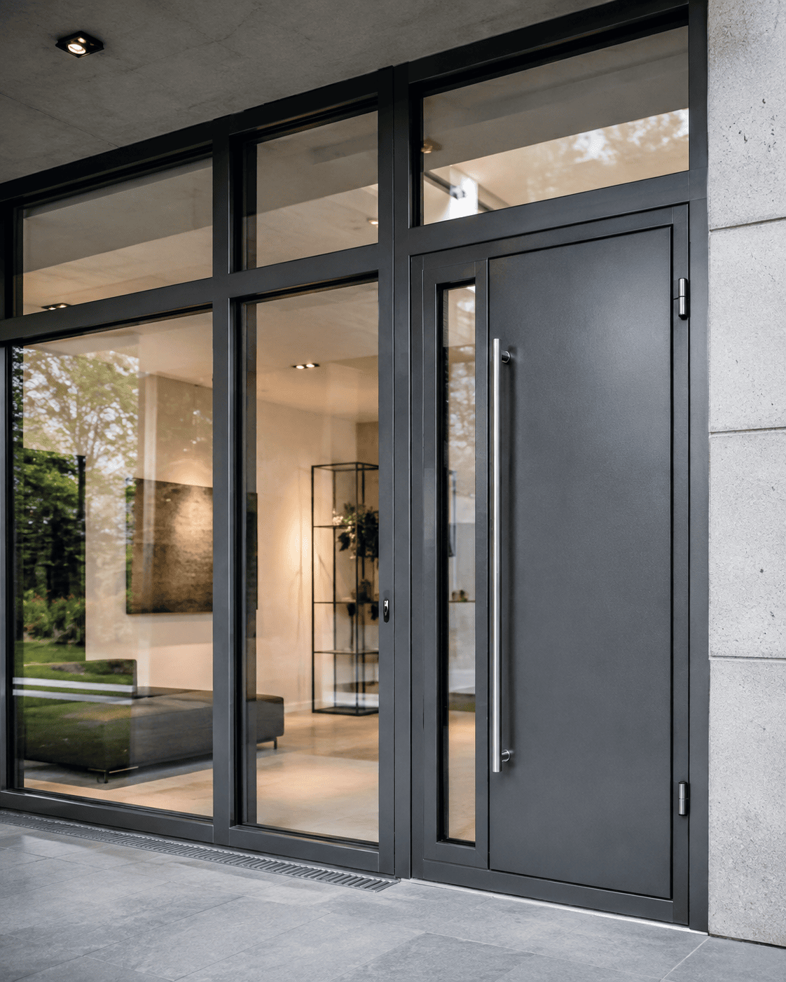 Moderne, dunkelgraue Eingangstür von Stahl- und Metallbau Drost mit vertikalem Edelstahlgriff, elegant in eine große Glasfassade integriert.