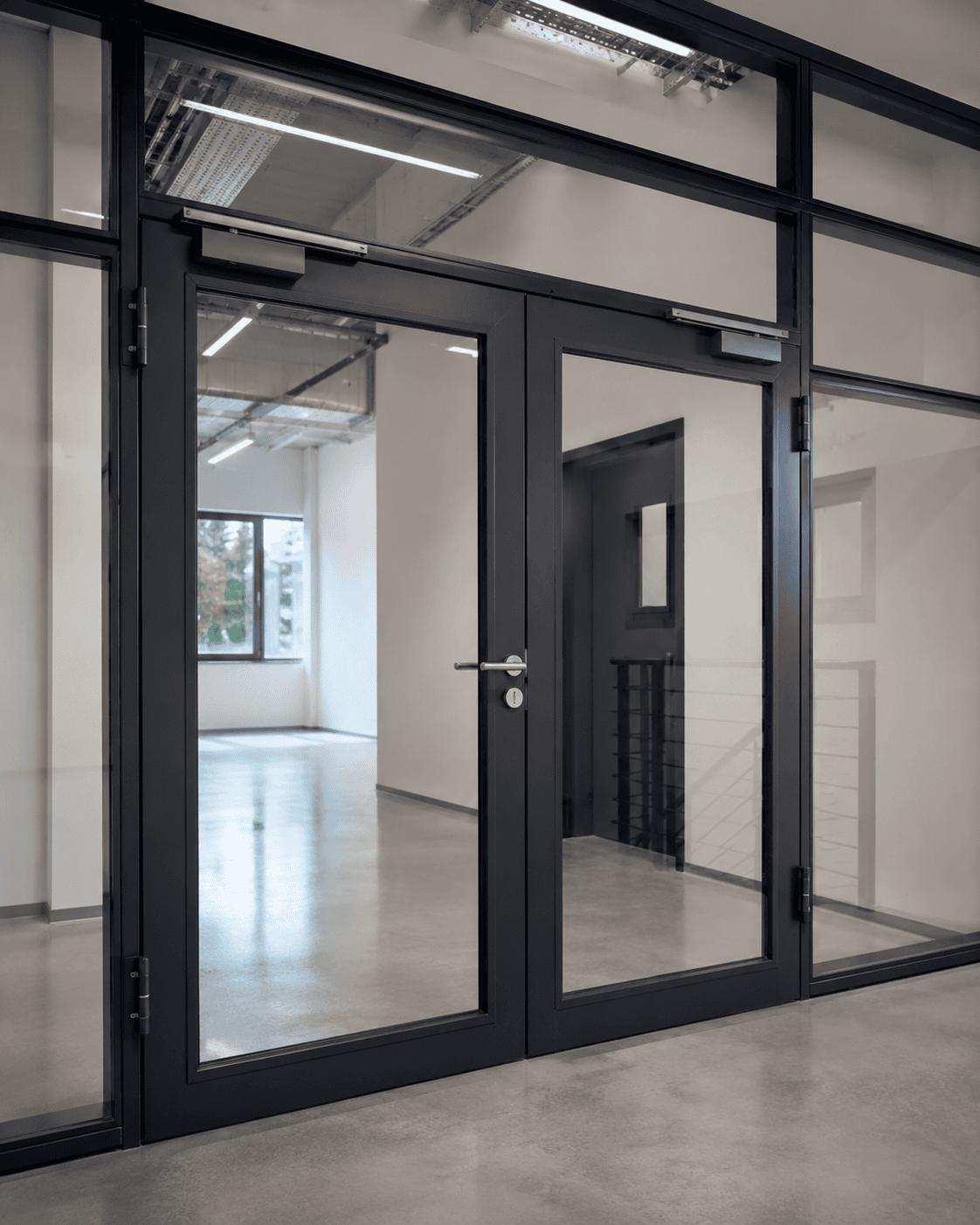 Moderne doppelflügelige Glastür mit anthrazitfarbenen Metallrahmen und festen Seitenteilen aus Glas, installiert von Stahl- und Metallbau Drost, in einem hellen Bürointerieur.