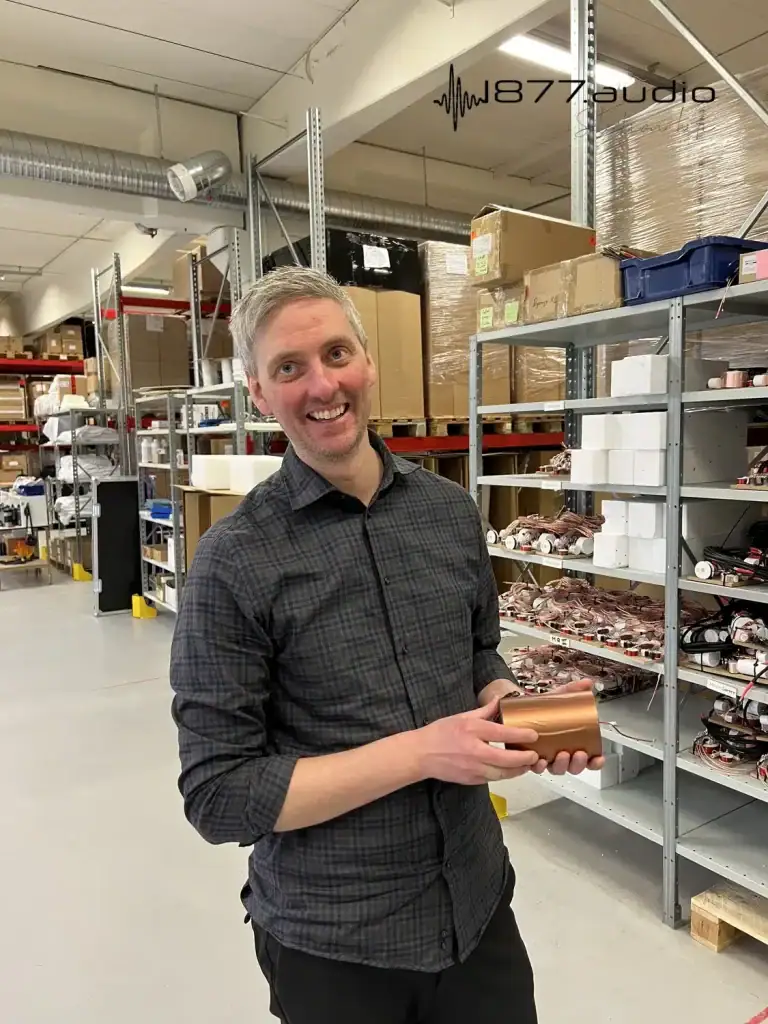 Mikael porte un condensateur en cuivre dans ses mains avec des racks de filtres dans des étagères en arrière-plan