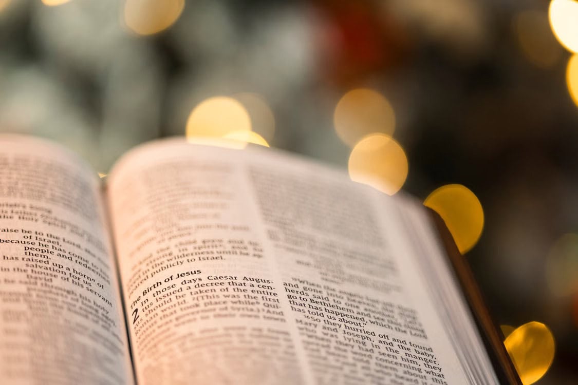 An open Bible on a table, softly lit by window light, with the page slightly out of focus.