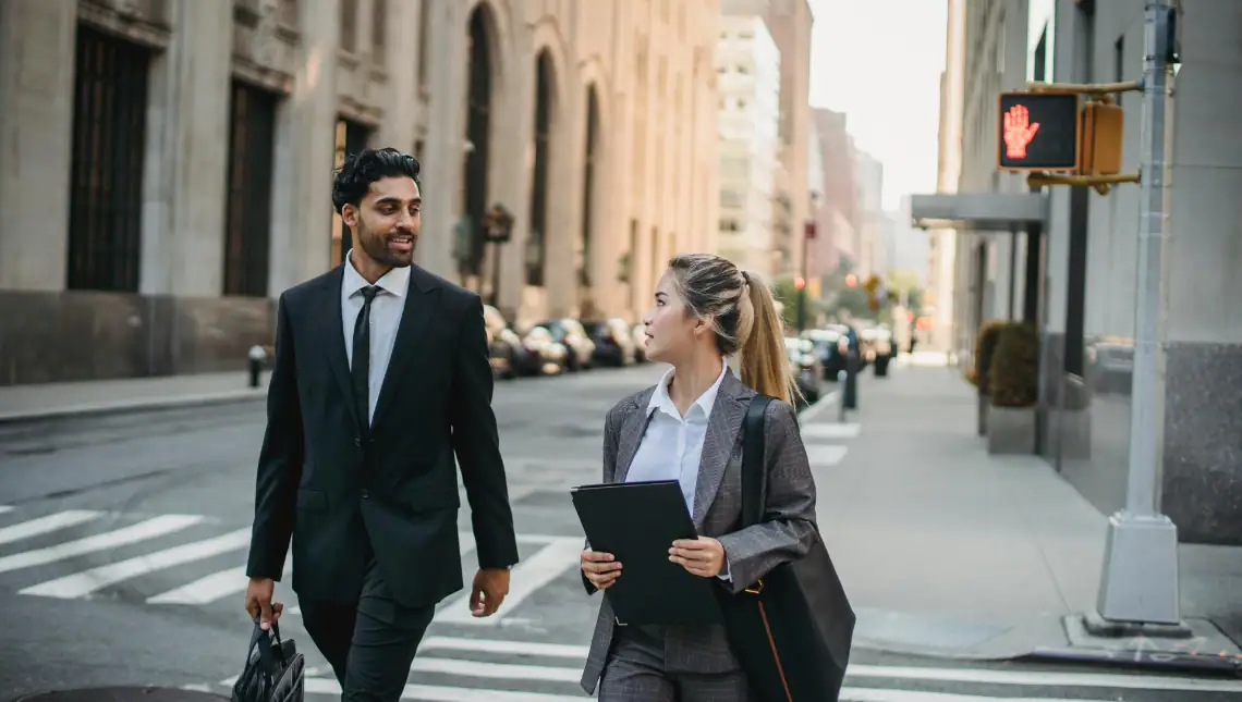 A man and woman in business attire looking at each other while crossing a street