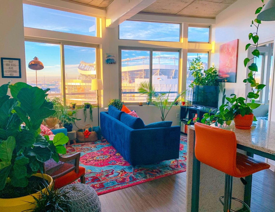 Modern apartment living room with a blue couch surrounded by lush greenery and stylish design accents showcasing contemporary apartment decor ideas for small spaces.