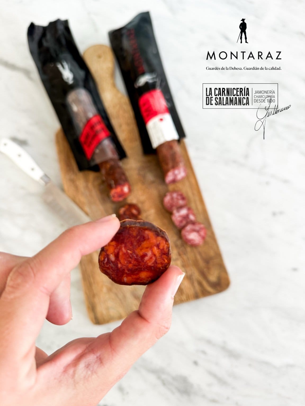 Mano sosteniendo una rodaja de chorizo vela Montaraz sobre tabla de madera con embutidos en La Carnicería de Salamanca