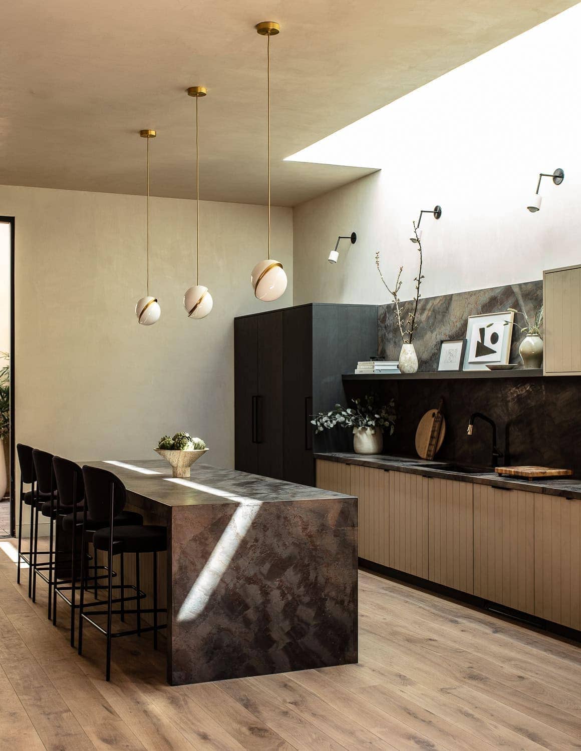 Stylish modern kitchen interior with black cabinetry, marble island, and pendant lighting.