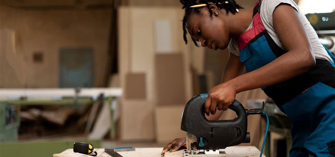 Young woman operating a jigsaw saw in a woodworking workshop.