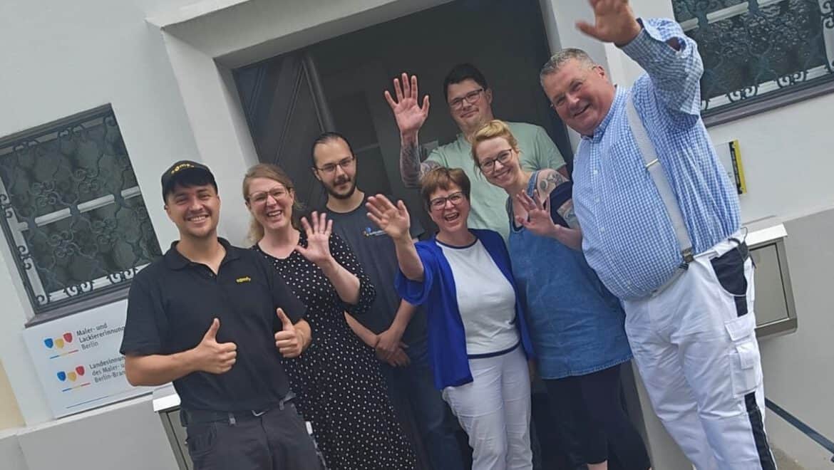 Gruppe von Menschen bei ITB Karlsruhe, lächelnd und winkend vor einem Gebäude.