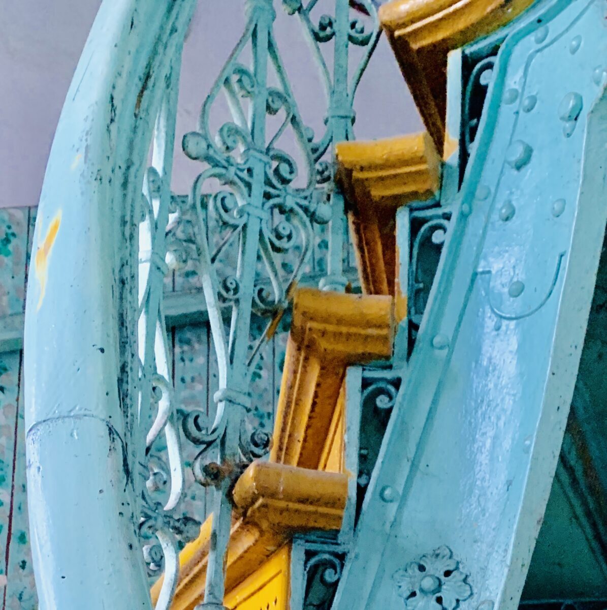 Ornate blue and yellow iron staircase with intricate detailing, highlighting vintage architectural design.