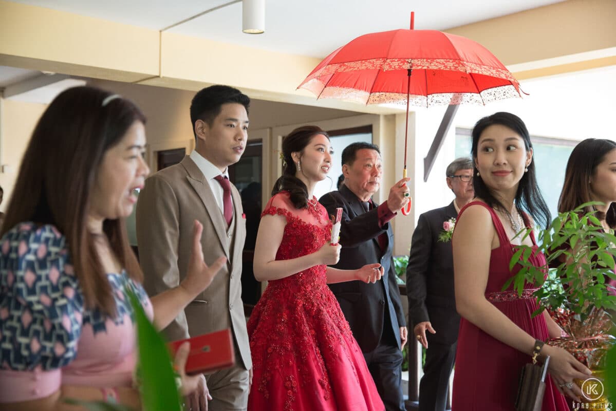 The bride in red leaves with her family under a red umbrella after the tea ceremony at Dusit Thani Hua Hin