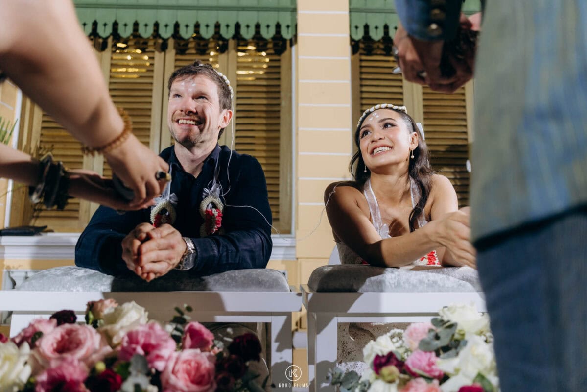 A guest pours water over the groom's hands as the couple laugh during the Thai water blessing at The House on Sathorn, W Bangkok