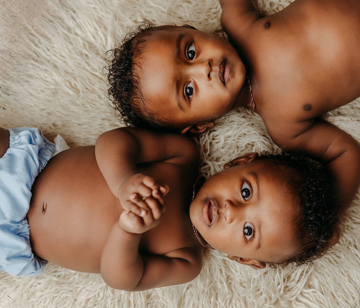 6 Months Milestone Photography Session with twin boys. They are laying on their backs on a fluffy rug and looking up at the camera