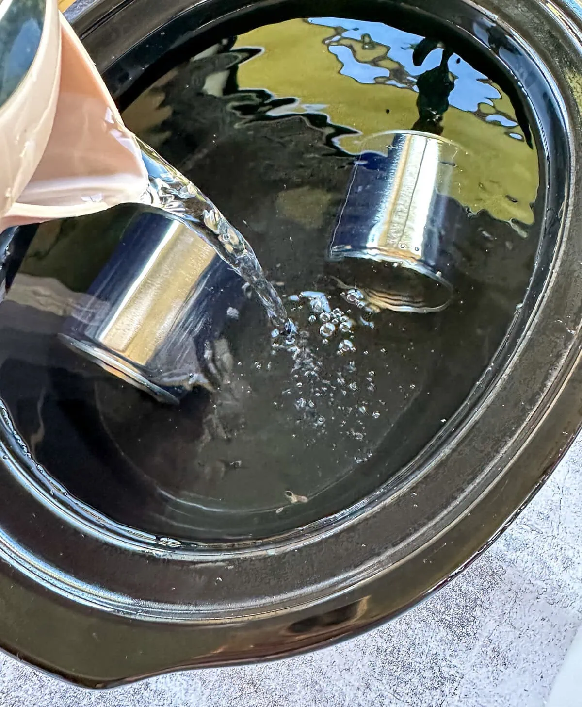 Pouring water into a slow cooker to completely cover the cans of condensed milk 