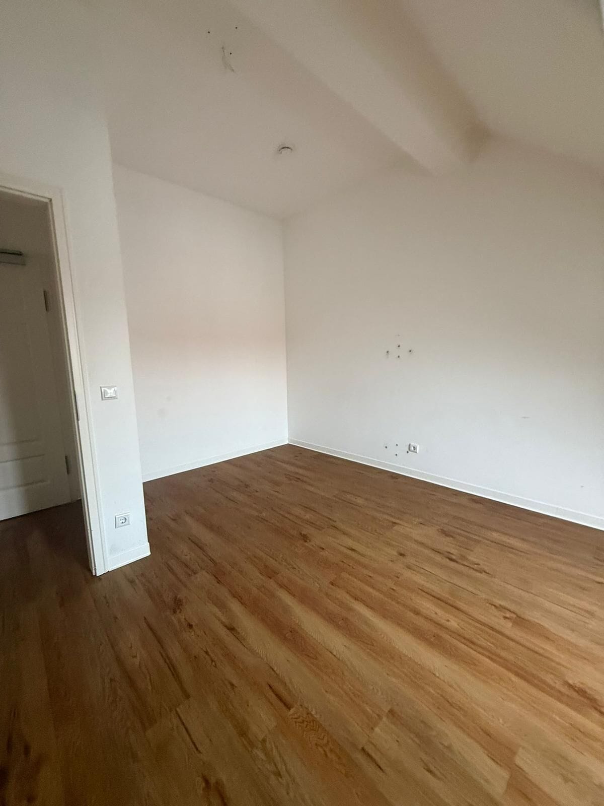 Der gleiche Raum nach der Entrümpelung. Leerer Holzboden, Balkontür, einzugsbereit.