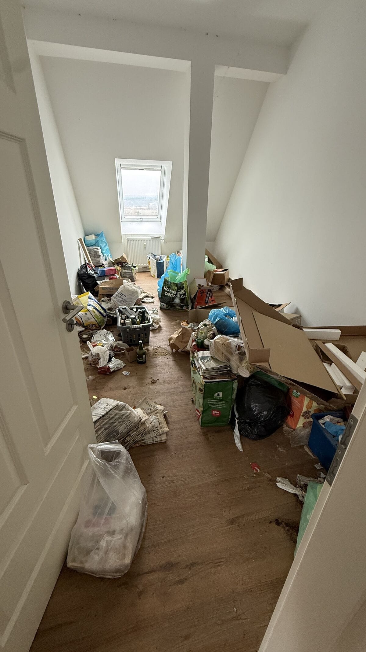 Eingangsbereich einer Dachgeschoss-Wohnung in Weimar vor der Entrümpelung. Korridor voller Kartons, Müllsäcke und Flaschen.