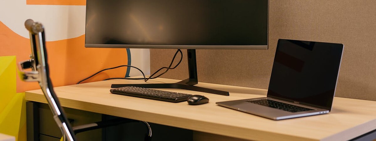 A modern office setup featuring a sleek computer monitor and a laptop on a wooden desk with a colorful abstract background.