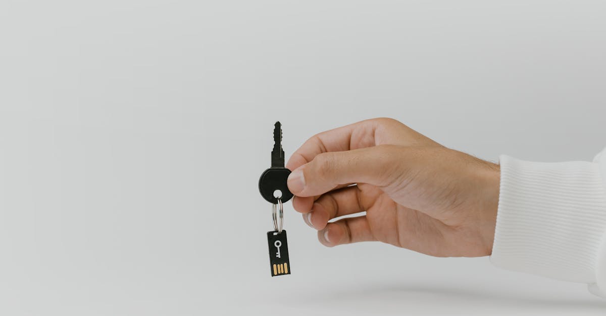 Hand holding keychain with integrated USB flash drive against a plain background.