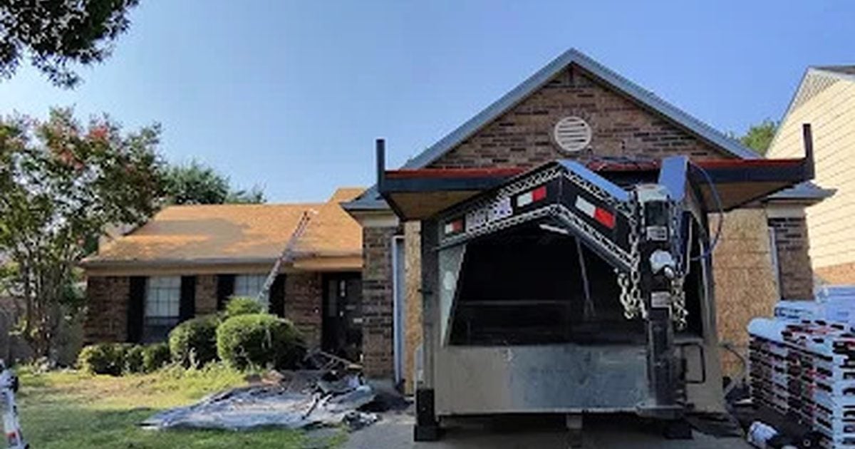 Roof replacement in progress at a DFW home, with a dump trailer in the driveway and shingle bundles staged on the lawn
