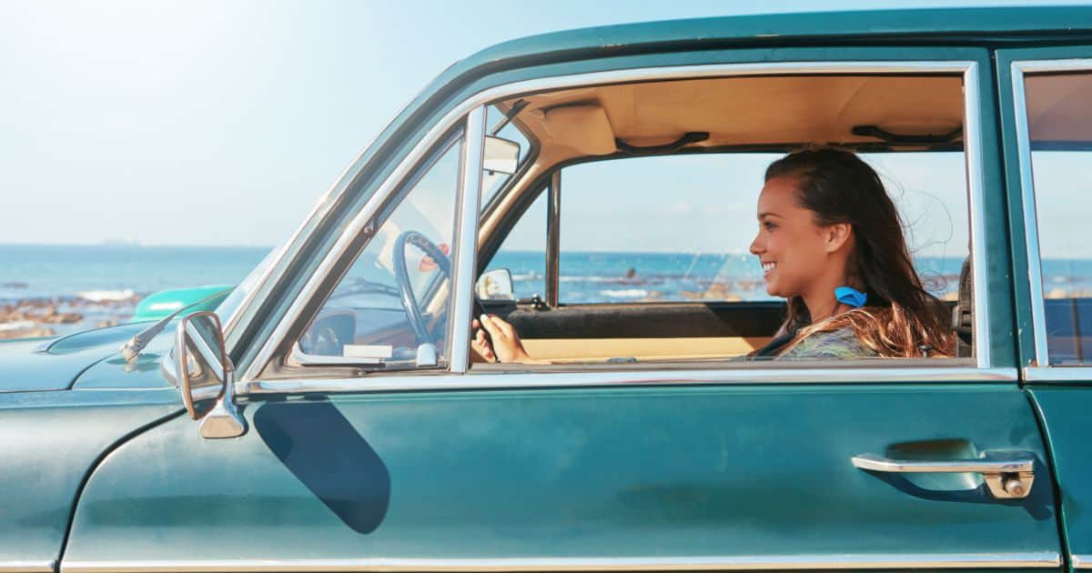 woman happy behind the wheel of a teal car she got while renting a car in puerto escondido