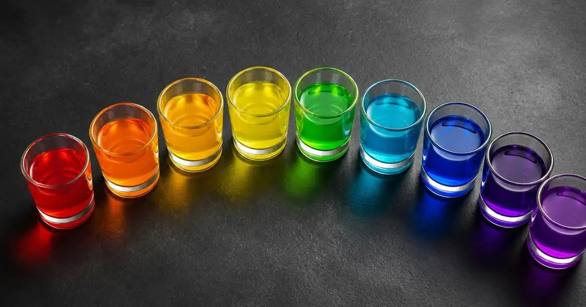 A curved row of small unlabelled cups holding brightly coloured liquids on a dark surface