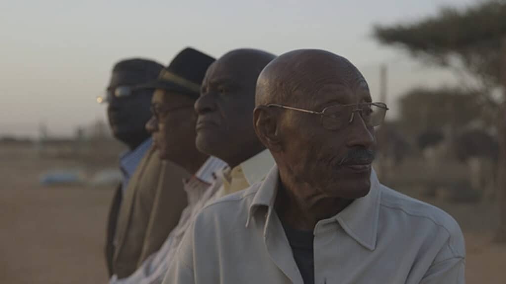 Still from Talking About Trees (2019) showing four elderly men looking into the distance at dusk, symbolising resilience and collective memory in Sudanese cinema.