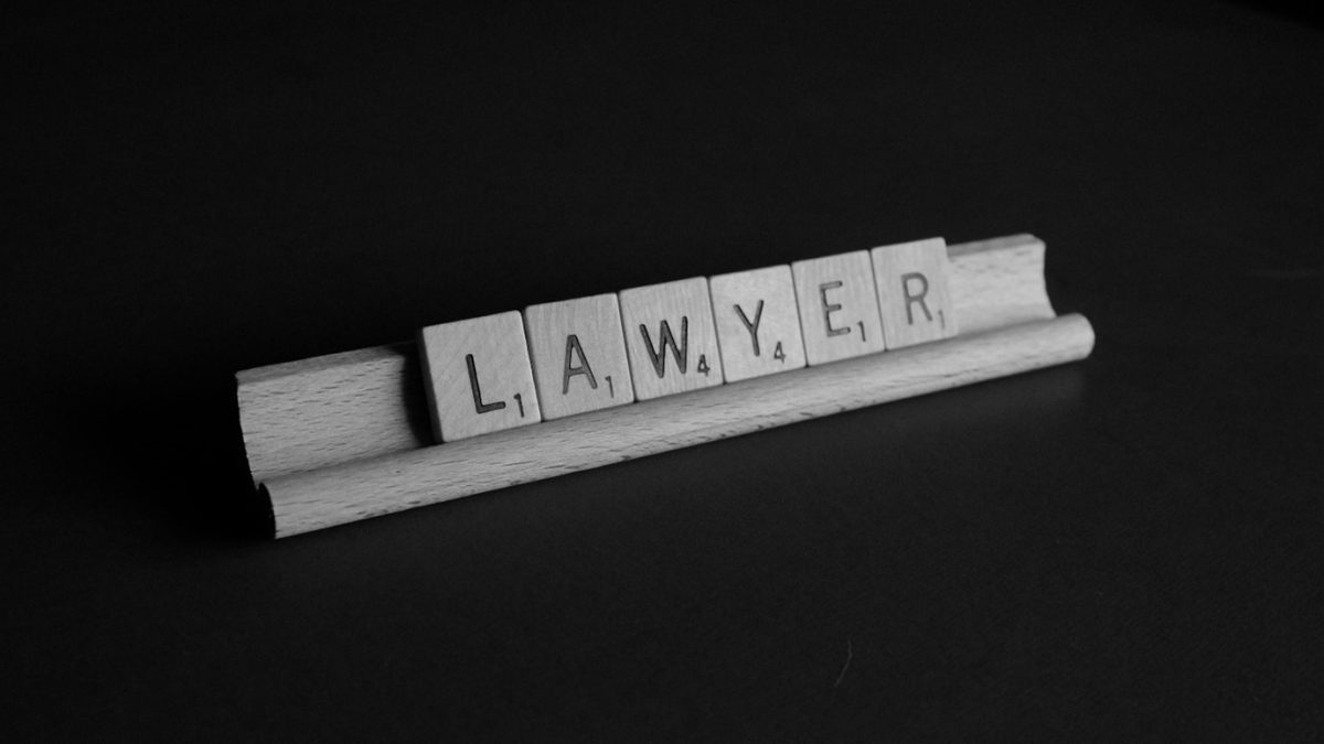 Scrabble tiles on a rack spelling out the word "LAWYER" against a black background.