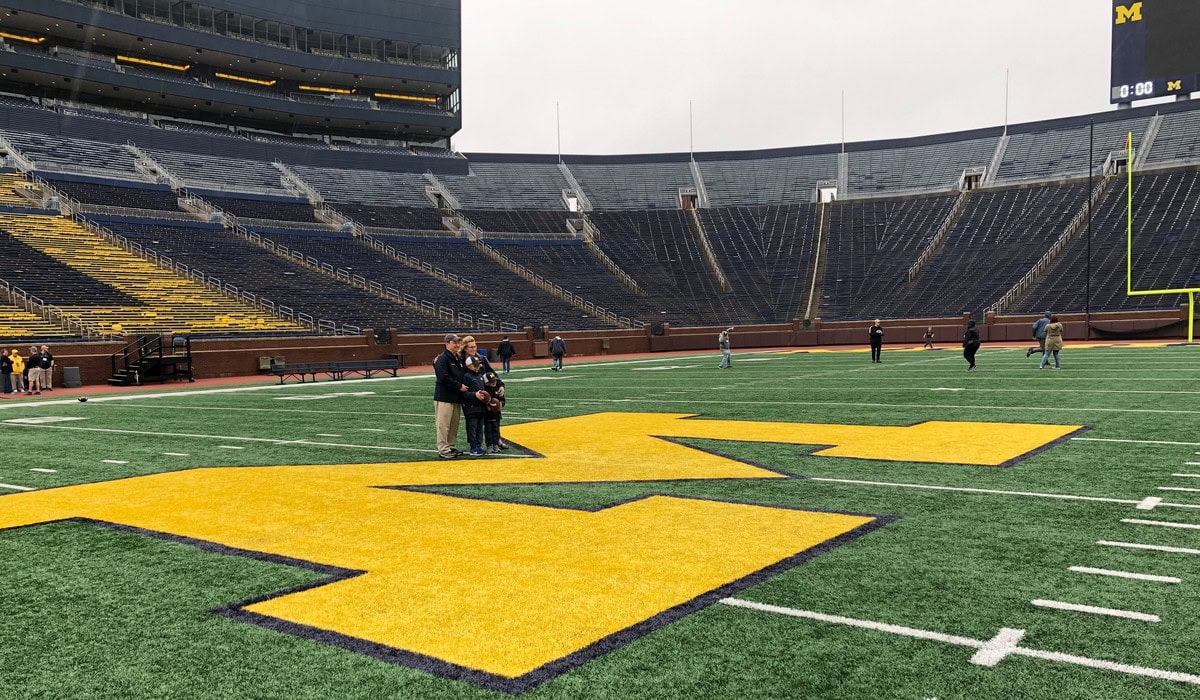 Fans take a photo at the 50-yard line of Michigan Stadium during a Big House Tour