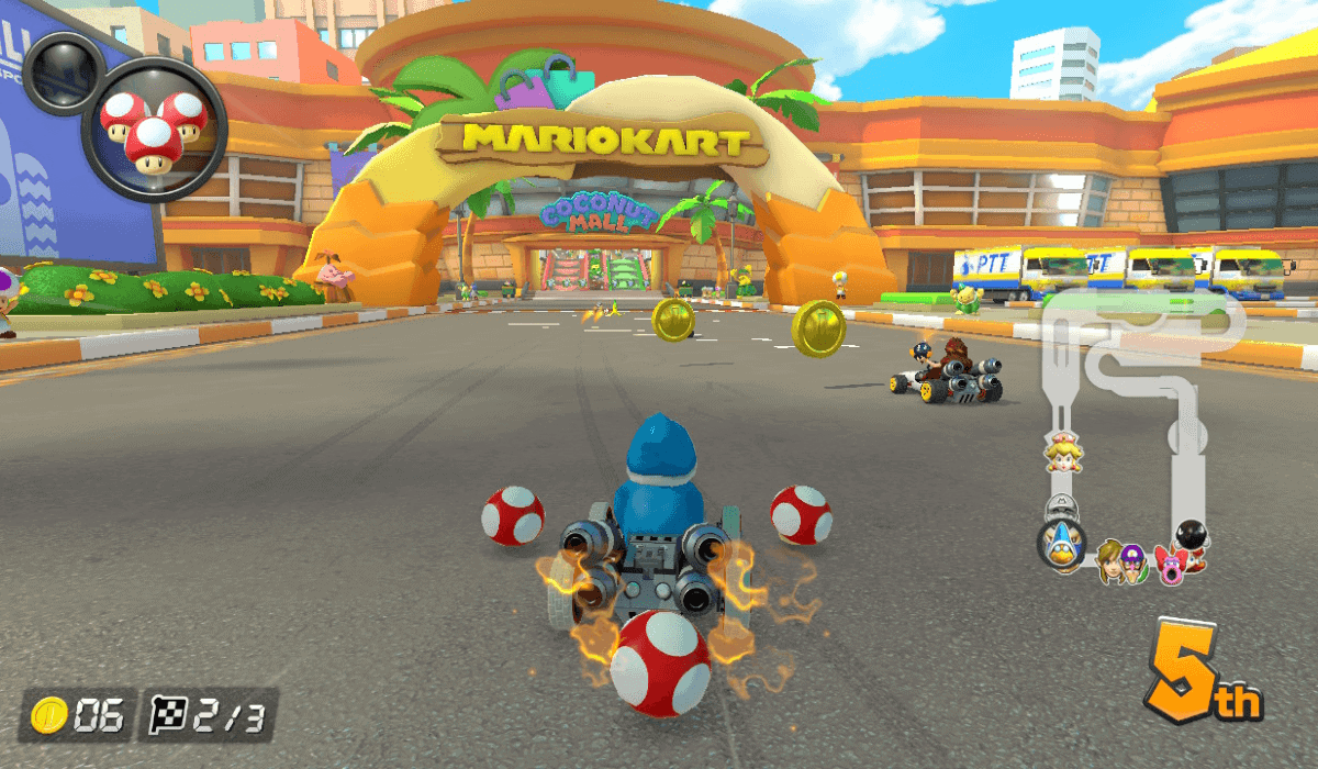 A screenshot of a race around Coconut Mall, a returning track added to Mario Kart 8 Deluxe by the Booster Course Pass. Racers are driving towards the finish line, which is just before the entrance to the eponymous mall.
