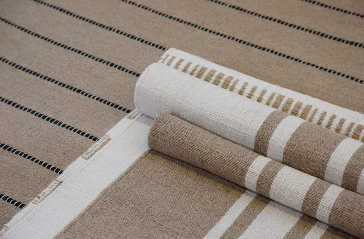 Close-up of beige striped area rug with layered sample swatches for interior decor styling.