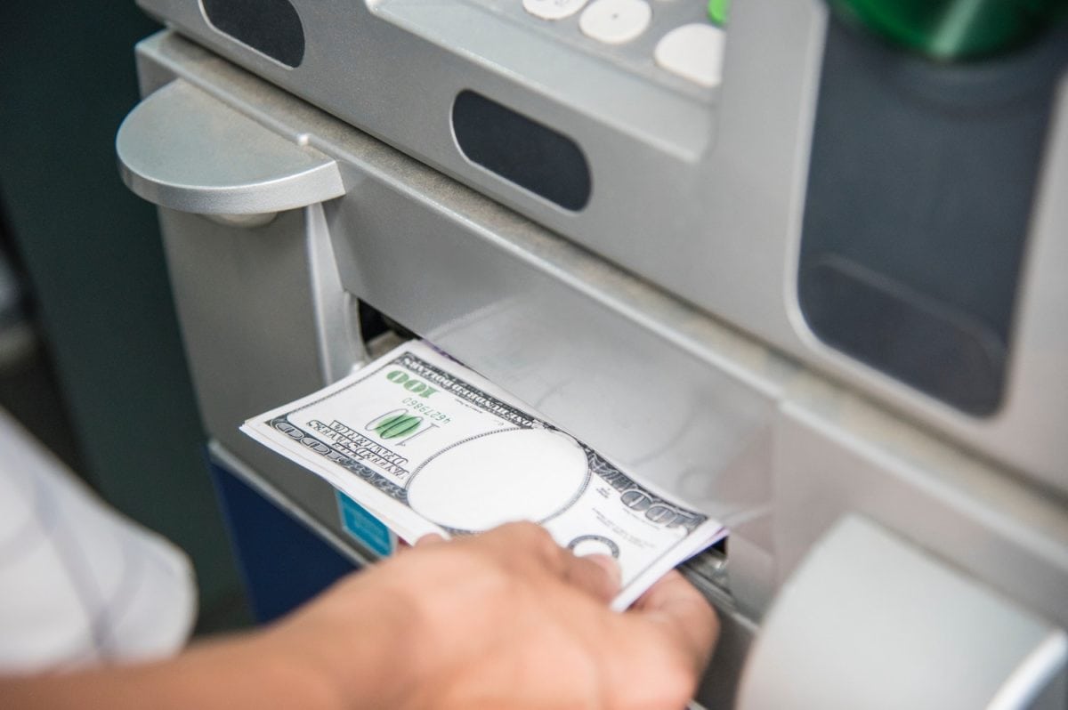 Person holt Geld aus einem Geldautomaten; sichtbar ist eine 100-Dollar-Note.