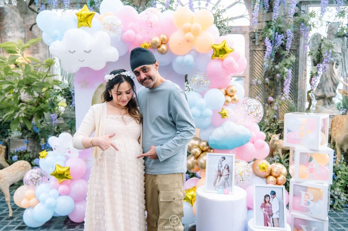Deepak and Joy, expecting their baby, pose by a pastel balloon arch at their gender reveal party at B-Story Garden Café, Bangkok