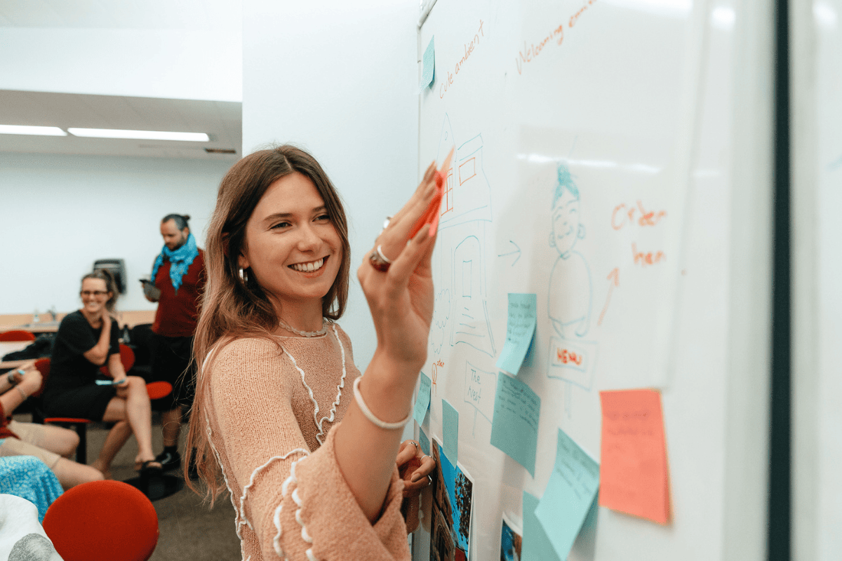 Additionally, the image features one of the ABC Silicon Valley 2024 participants placing a post-it note on a board as she collaborates on startup ideas with her team.