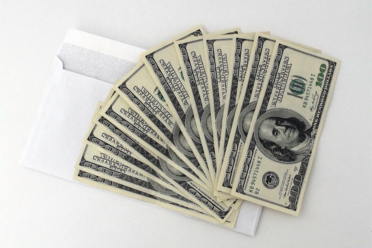 Mehrere 100-Dollar-Scheine fächerförmig auf einem weißen Umschlag ausgelegt.