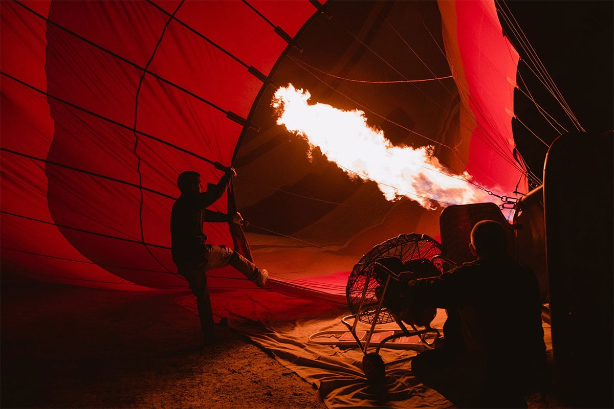 Ein Heißluftballon wird nachts mit einer großen Flamme aufgeheizt, während Menschen daran arbeiten.